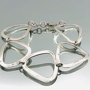 May include: A silver bracelet with a geometric design. The bracelet is made of five interlocking pieces, each shaped like a teardrop. The bracelet is open and has a clasp.
