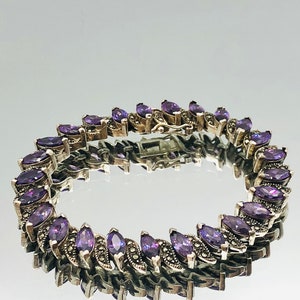 May include: A silver bracelet with a row of marquise-shaped purple gemstones and a silver clasp.