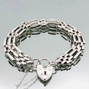Puede incluir: Un brazalete de cadena de plata con un cierre de candado en forma de corazón. El brazalete está hecho de múltiples filas de formas rectangulares enlazadas.