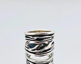 May include: A silver ring with a textured, wavy design. The ring is wide and has a unique, organic look.