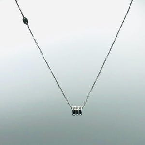 May include: A silver necklace with a delicate chain and a pendant featuring three small, cylindrical silver beads. The necklace is displayed against a light gray background, highlighting its minimalist design.