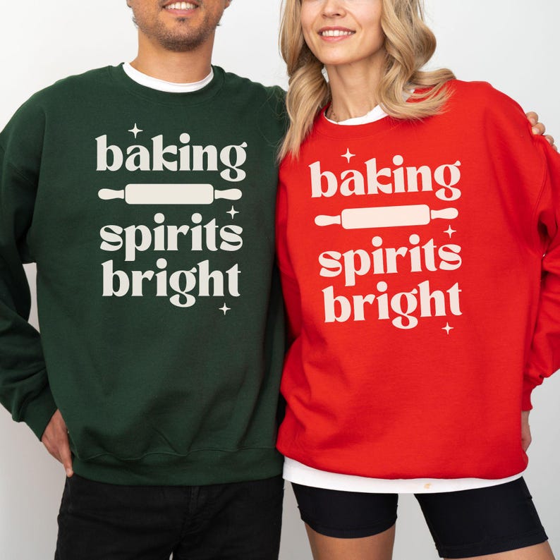 K&ouml;nnte beinhalten: Ein dunkelgr&uuml;nes Sweatshirt und ein leuchtend rotes Sweatshirt, beide mit dem wei&szlig;en Schriftzug "baking spirits bright" und einer Nudelholz-Grafik. Das Design enth&auml;lt kleine vierzackige Sterne oberhalb und unterhalb des Textes.