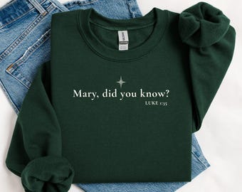 Könnte beinhalten: Dunkelgrünes Sweatshirt mit dem weißen Text "Mary, did you know?" und "Luke 1:35". Über dem Text befindet sich eine Sternengrafik. Das Sweatshirt liegt gefaltet auf einer blauen Jeans.