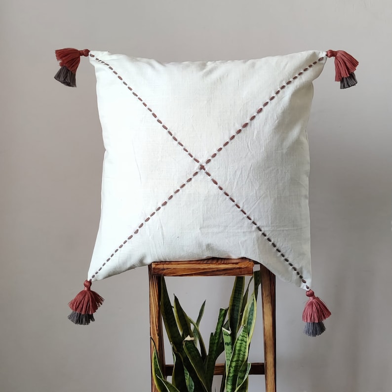 This is a 100% cotton cushion in off white color with minimalist and subtle geometric cross pattern hand embroidery and finished with double tassels on each corner. The tassels are earthy tones of color grey and brown. Size - 50x50 cm