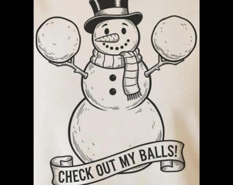 May include: Black and white illustration of a snowman wearing a top hat and scarf, holding two snowballs. The banner below reads "CHECK OUT MY BALLS!" A humorous winter-themed design.
