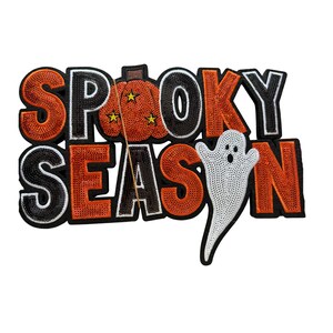 May include: A decorative patch featuring the text SPOOKY SEASON in orange and black sequins. The letter O in SPOOKY is replaced by an orange pumpkin with three small yellow stars, and a white sequined ghost is positioned over the letter O in SEASON.