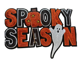 May include: A decorative patch featuring the text SPOOKY SEASON in orange and black sequins. The letter O in SPOOKY is replaced by an orange pumpkin with three small yellow stars, and a white sequined ghost is positioned over the letter O in SEASON.