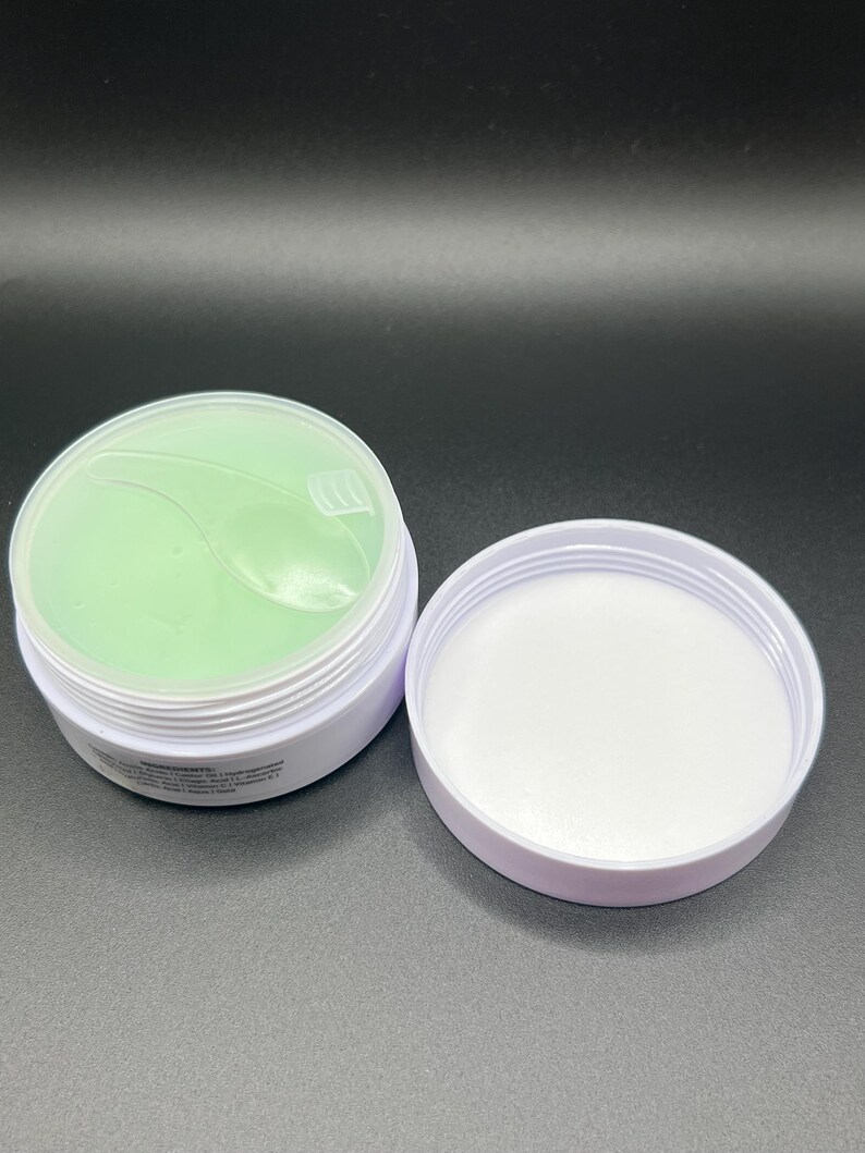 May include: Open white container with a light green gel product inside. The lid is off, revealing the product and the white interior of the container. The product appears to be a skincare item, possibly eye patches.