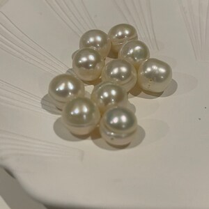 May include: A group of white pearls on a white surface. The pearls are round and smooth, and they are arranged in a cluster.