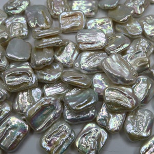 May include: A collection of white, iridescent, rectangular-shaped freshwater pearls. The pearls have a smooth, polished surface and a slightly irregular shape.