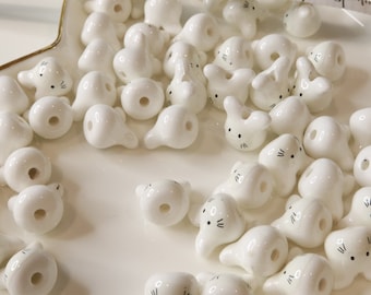 May include: A collection of white ceramic bunny beads with black painted eyes and whiskers. The beads have a hole in the center for stringing.