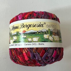May include: A skein of red, orange, purple, and gold yarn with a label that reads "Lane Borgosesia dal 1850" and "Carisio (VC) - Biella".