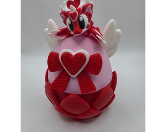 May include: A 3D-printed figurine of a dragon-like creature with a heart-shaped head and wings. The figurine is primarily red and white, with a pink body and a red bow. The base is red and petal-shaped.