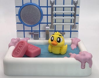 May include: A miniature bathroom scene featuring a yellow duck in a bathtub with pink soap and bubbles. The background has a blue and white tiled wall with a mirror and a towel rack. The soap bars are pink and have the word "SOAP" printed on them.