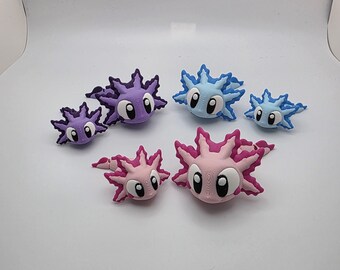 May include: A collection of six axolotl figurines in varying sizes and colors, including purple, light blue, and pink. Each creature features large white eyes with black pupils, spiky external gills, and a smooth, rounded body shape.