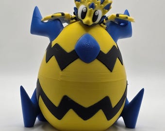 May include: A 3D-printed figure of a cartoon character with a yellow body, black zig-zag stripes, and blue accents. The figure has a large, egg-shaped body and a smaller head with large eyes. The figure is sitting on a white surface.