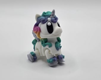 May include: A white unicorn figurine with a colorful mane and tail. The unicorn has a teal, purple, and yellow mane, with matching accents on its hooves. The unicorn has large black eyes and a small gray horn.