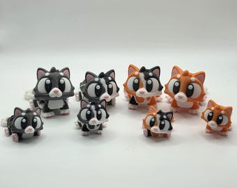 May include: A collection of small, cartoon-style cat figurines in various colors, including gray, black, orange, and white. The cats have large eyes and pink paws. The figurines are arranged on a white surface.
