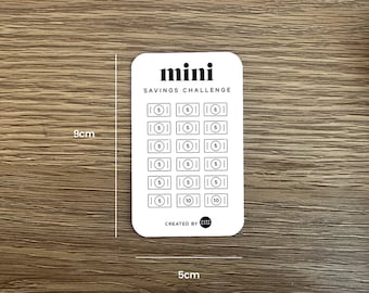 May include: A white card with the text "mini savings challenge" printed in black. The card has a grid of 20 circles, each with a dollar sign and a number inside. The numbers are 5 and 10. The card is 5 cm by 9 cm.