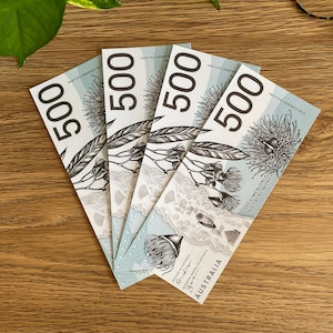 May include: Four Australian $500 notes fanned out on a wooden surface. The notes feature a floral design with the text "SPECIMEN ONLY NOT LEGAL MONEY" printed on the bottom right corner.
