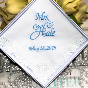 May include: A white handkerchief with lace trim, embroidered with the text "Mrs. Hale" and the date "May 18, 2019" in blue thread. The handkerchief is in a white box.