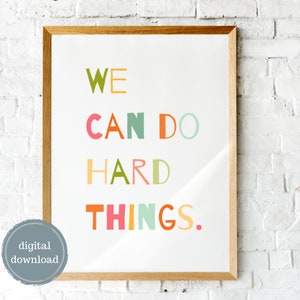 May include: A framed print with the text "WE CAN DO HARD THINGS." in colorful letters on a white background. The frame is wood with a light brown finish.