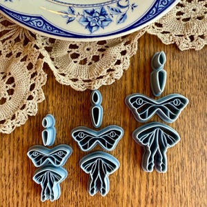 May include: Set of four grey plastic butterfly cookie cutters. The cutters are in different sizes and feature a detailed butterfly design.