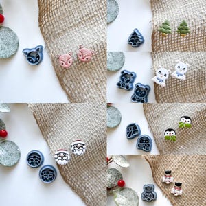 May include: A collection of Christmas-themed cookie cutters in various shapes and colors, including a reindeer, a penguin, a snowman, a Santa Claus, a tree, and a bear. The cutters are made of blue and white plastic and are arranged on a burlap background.