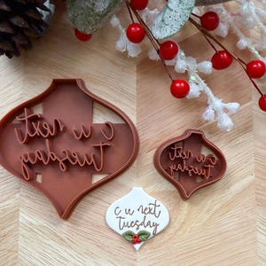 Può includere: Tagliapasta in plastica marrone a forma di ornamento con la scritta "it's w next Tuesday" e un ornamento bianco con la scritta "c u next Tuesday" e bacche di agrifoglio. Strumenti di cottura festivi.