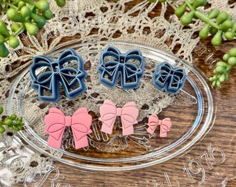 May include: A set of six bow-shaped cookie cutters in two different sizes. The larger cutters are blue and the smaller cutters are pink.
