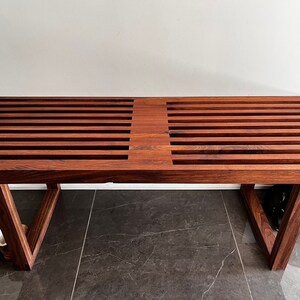 May include: A dark brown wooden bench with a slatted top and a simple, rectangular frame. The bench is made of solid wood and has a natural finish.