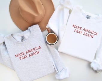 Può includere: Due felpe con il testo "Make America Pray Again" in lettere rosse. Una felpa è grigia e l'altra è bianca.