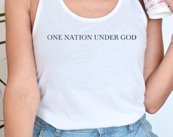 Può includere: Canotta bianca con la scritta "ONE NATION UNDER GOD" in nero. La canotta è abbinata a pantaloncini di jeans blu chiaro. Una persona tiene in mano una tazza di caffè con un disegno di palma.