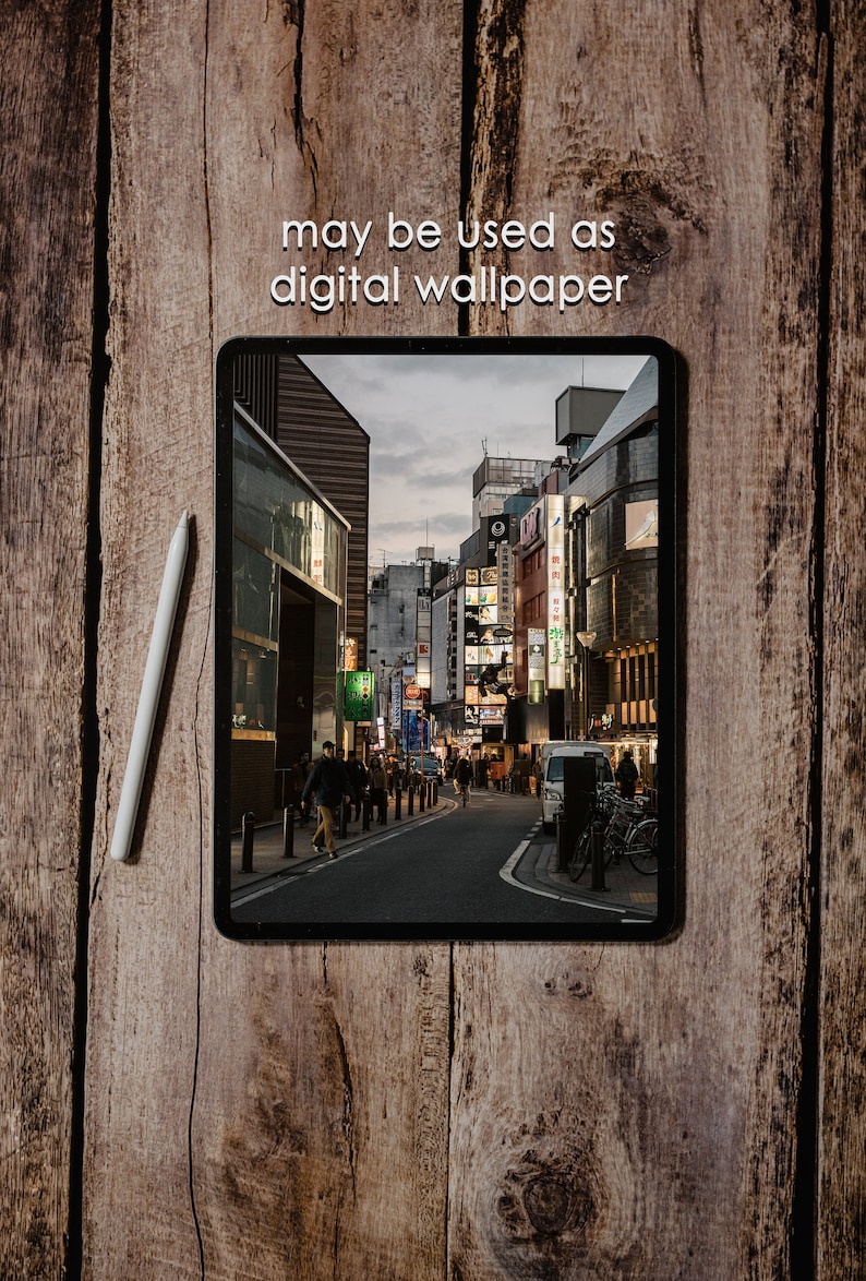 May include: A digital tablet displaying a photo of a street in a city with buildings and people walking. The text "may be used as digital wallpaper" is displayed above the tablet.