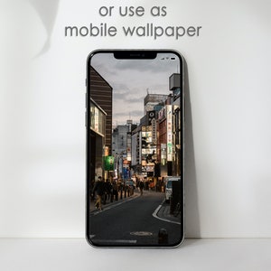 May include: A smartphone displaying a photo of a city street at night. The street is lined with buildings and streetlights. People are walking on the sidewalk. The text "or use as mobile wallpaper" is displayed above the phone.
