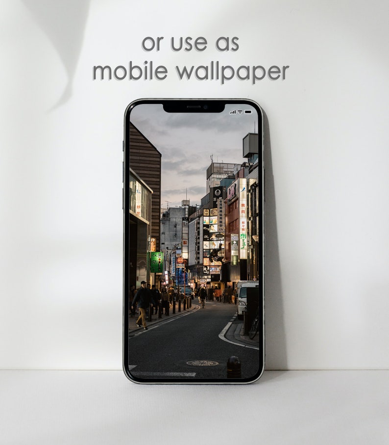 May include: A smartphone displaying a photo of a city street at night. The street is lined with buildings and streetlights. People are walking on the sidewalk. The text "or use as mobile wallpaper" is displayed above the phone.