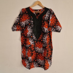 Peut inclure: Une chemise à manches courtes noire et orange avec un motif floral blanc et noir. La chemise a un col en V et une bordure en dentelle noire.