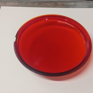 May include: A round, red glass ashtray.