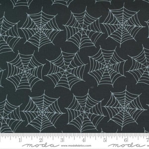 May include: Black fabric with a white spiderweb pattern. The fabric is 17.8 cm wide and has a ruler for scale.