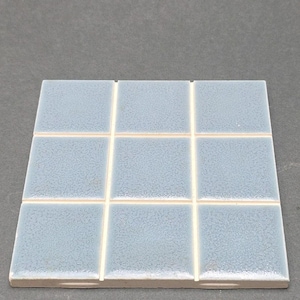 May include: A square of nine light blue ceramic tiles with white grout lines. The tiles have a textured surface and are arranged in a grid pattern. The tiles are likely for use in a bathroom or kitchen.