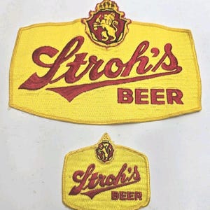 May include: Two yellow embroidered patches with the Stroh's Beer logo. The larger patch features the brand name in red script above the word "BEER". A smaller patch with the same design is below.