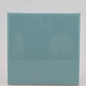 May include: A square, solid-color tile in a muted teal hue. The tile has a glossy finish and a smooth, even surface. The edges are slightly rounded. This tile is suitable for various home decor projects.