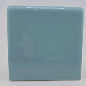 May include: A square, light blue ceramic tile with rounded edges. The tile has a glossy finish and a solid color. The tile is a solid, square shape, and is likely for use in a bathroom or kitchen.