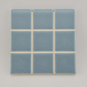 May include: Nine square, textured, light blue tiles arranged in a 3x3 grid. The tiles are separated by thin, off-white grout lines. The tiles have a slightly speckled appearance, and the overall aesthetic is clean and modern.