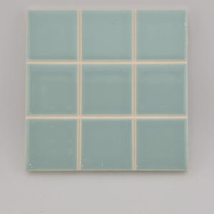 May include: A square of nine light blue ceramic tiles arranged in a grid pattern. The tiles have a glossy finish and are separated by thin, off-white grout lines. The tiles are a solid, muted blue-green color.