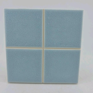 May include: Four square, light blue tiles arranged together. The tiles have a textured surface and are separated by thin, off-white grout lines. The tiles are a muted, pastel blue color.