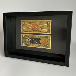 Peut inclure: Deux billets de banque Litecoin Reserve Notes dorés encadrés dans un cadre noir. Le billet du haut indique "Litecoin Reserve Note Peer-to-Peer" et le billet du bas indique "Litecoin Reserve Note".