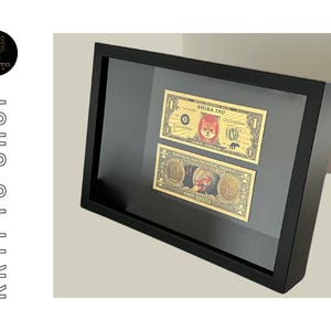 Peut inclure: Une image encadrée noire contenant deux billets de crypto-monnaie Shiba Inu de couleur dorée. Les billets représentent un chien Shiba Inu et le texte "Shiba Inu" et "One Shiba".