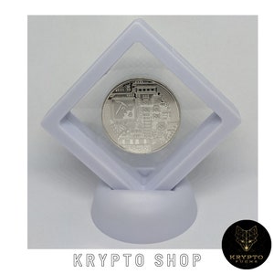 May include: A silver-colored cryptocurrency coin with a circuit board design and a pickaxe symbol is displayed in a clear plastic square display case on a white stand. The stand is on a white background. The text "KRYPTO SHOP" is printed below the stand.