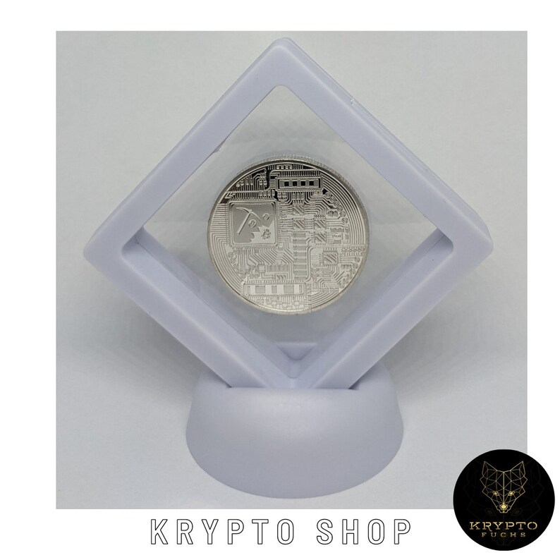 May include: A silver-colored cryptocurrency coin with a circuit board design and a pickaxe symbol is displayed in a clear plastic square display case on a white stand. The stand is on a white background. The text "KRYPTO SHOP" is printed below the stand.
